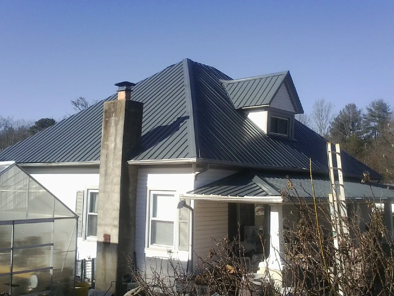 Dark blue standing seam metal roof on a white farmhouse with dormer — Slate & Tile Roof Repair by Roofing Brothers in Hartstown
