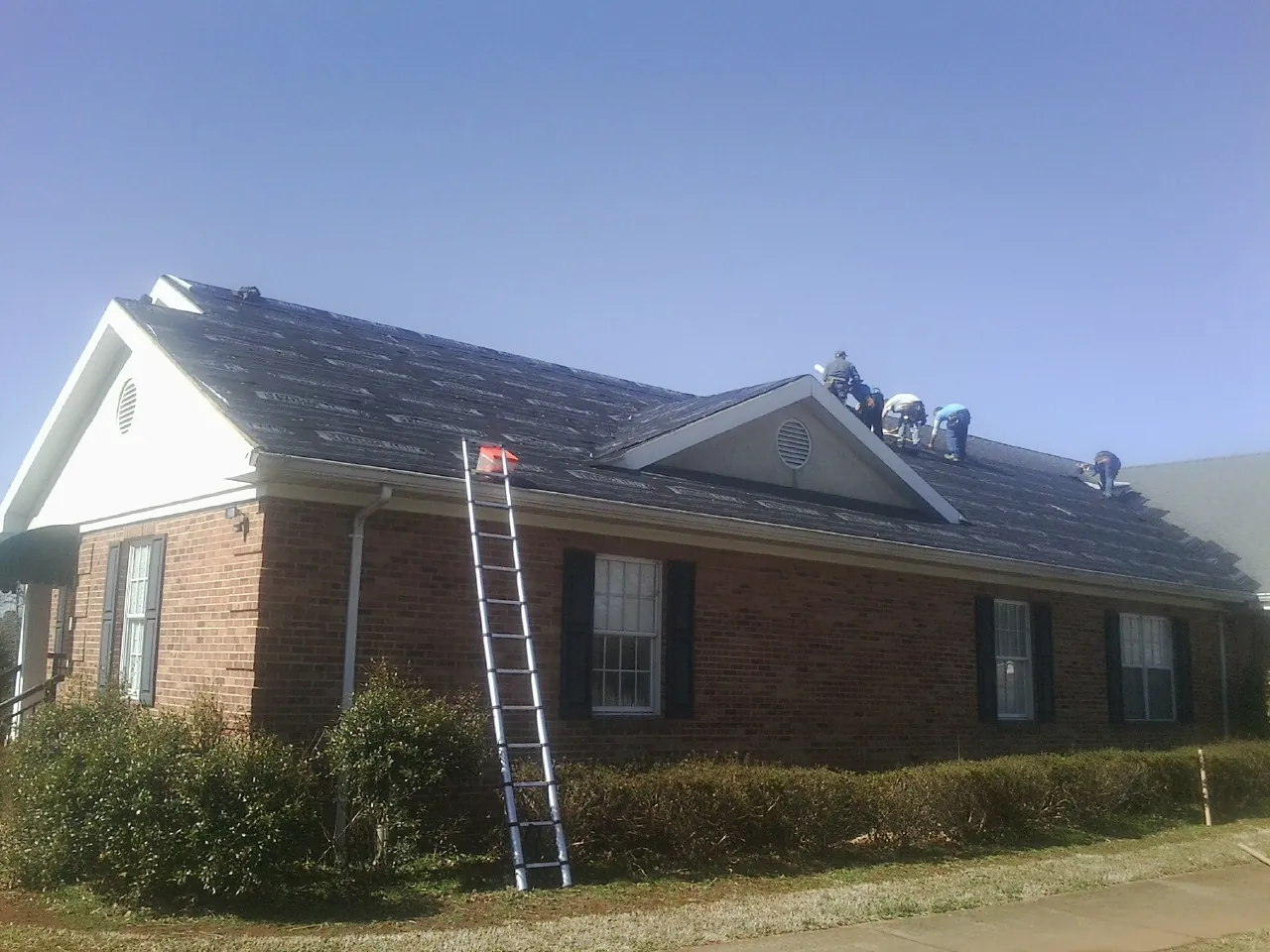 Crew tearing shingles off a brick ranch roof with a ladder set — Emergency Roof Repair work by our crew in Hartstown