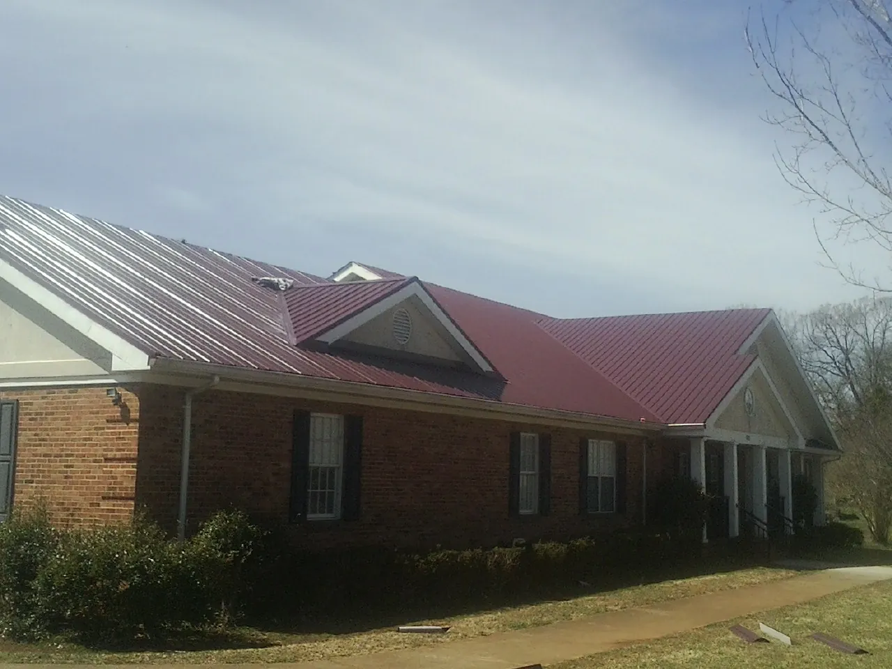 Red metal roof with gabled entries on a long brick building, from a Hail Damage Roof Repair job in Hartstown