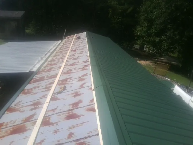 Old rusted panels beside newly installed green metal roofing — Wind Damage Roof Repair by Roofing Brothers in Hartstown