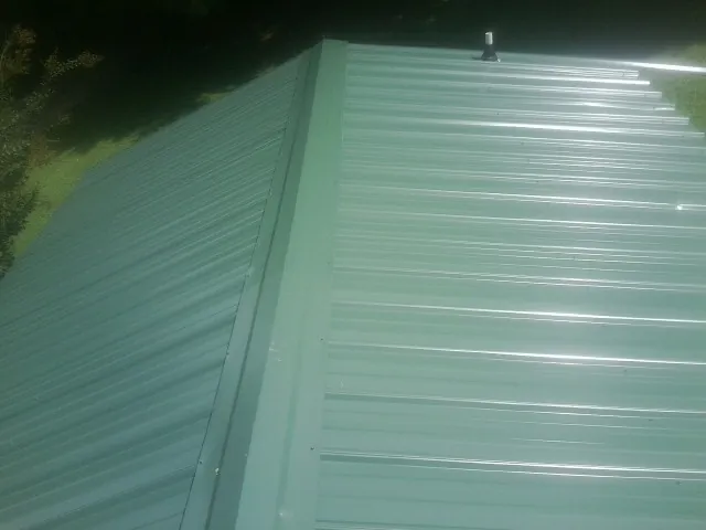New green metal panels meeting at the ridge of a roof — Flat Roof Repair work by our crew in Hartstown