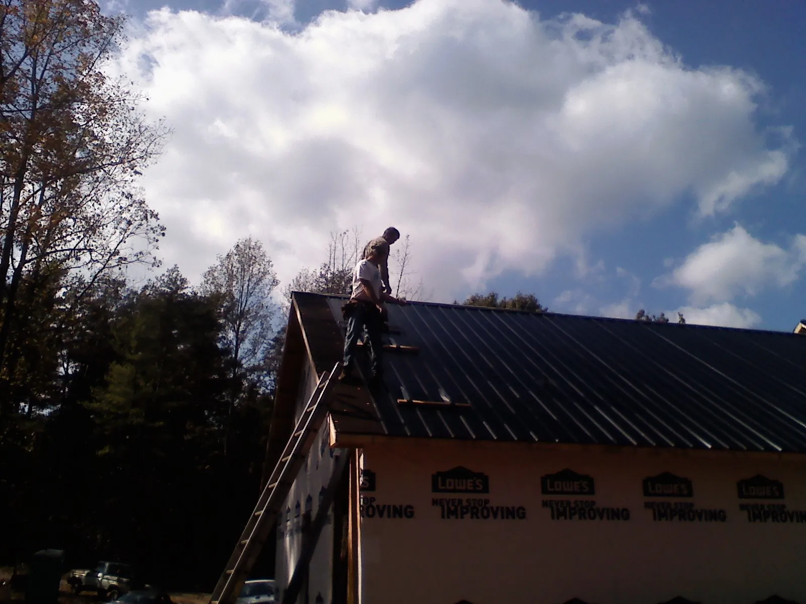 Roofer fastening dark metal panels high against a cloudy sky in Hartstown