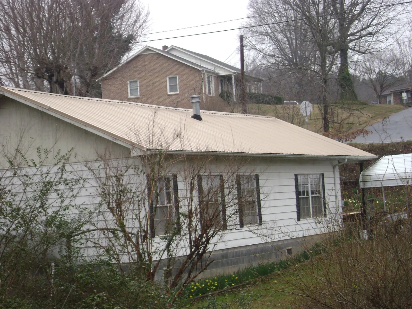 Tan metal roof on a white sided house set into a hillside — Commercial Roofing by Roofing Brothers in Hartstown
